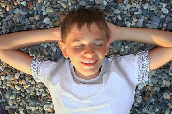 Teenager boy lying on stones on stone seacoast, closed eyes, hol — Stock Photo, Image
