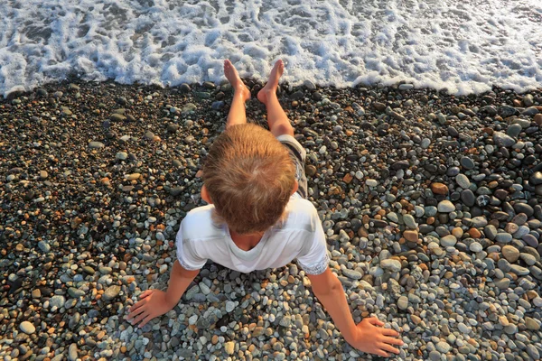 Sitter tonåring pojke på sten seacoasten, kissar fötter i vatten, sitt — Stockfoto