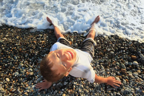 Yukarı doğru taş sahil, wets ücreti arayan genç oğlan oturuyor — Stok fotoğraf