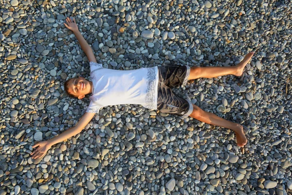 Dospívající chlapec leží na kamenech na kamenné seacoast — Stock fotografie