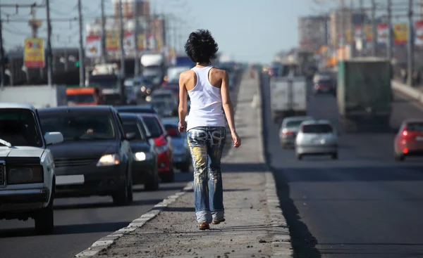 Flicka går på motorvägen mitt i city, vy från baksidan — Stockfoto