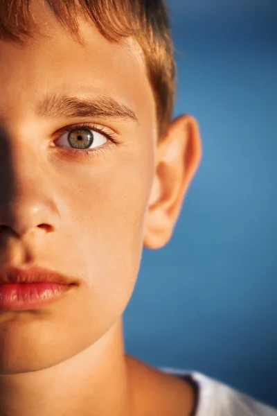 Překvapený dospívající chlapec proti moři, polovinu obličeje — Stock fotografie