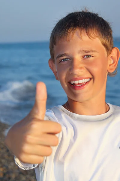 Sonriente adolescente chico contra mar muestra gesto — Foto de Stock