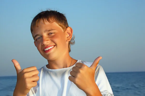 Sorrindo adolescente menino contra mar mostra gesto — Fotografia de Stock