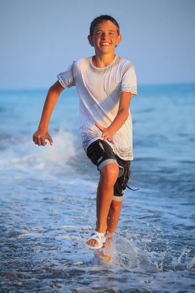 Tonåring pojke körs i våta kläder på stranden — Stockfoto
