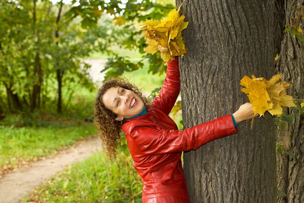 Молодая женщина с кленовыми листьями в руках возле дерева в лесу на ауту — стоковое фото