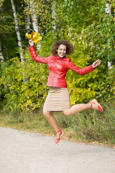 Jovem mulher com folhas nas mãos em salto em madeira no outono — Fotografia de Stock