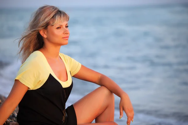 Сидящая красивая молодая женщина на берегу моря — стоковое фото