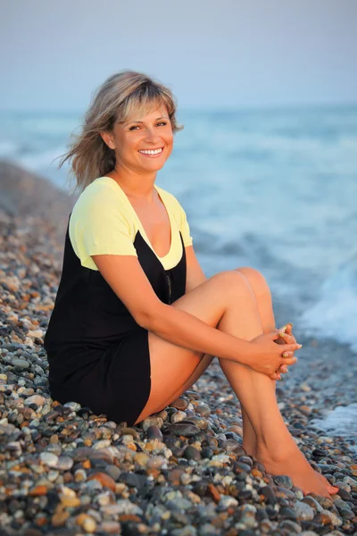 Sitting smiling beautiful woman on stone seacoast — Stock Photo, Image