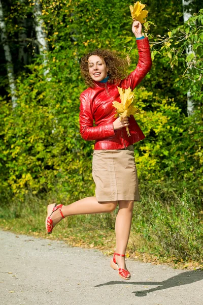Mladá žena s listy v rukou ve skoku v lese na podzim — Stock fotografie