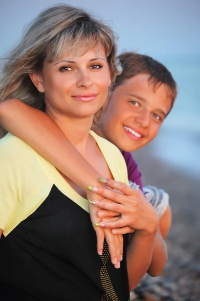Усміхнений хлопчик обіймає молоду жінку на пляжі ввечері — стокове фото