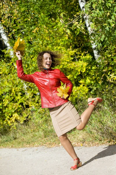 Giovane donna con foglie in mano in salto in legno in autunno — Foto Stock