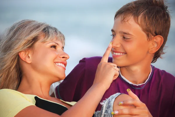 Young woman touches with finger nose of smiling boy in evening, — Stock Photo, Image