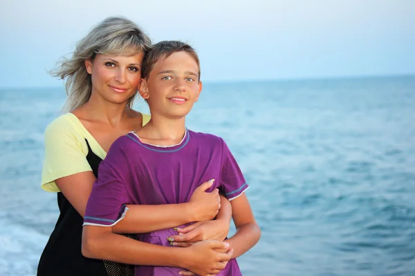 Молодая женщина обнимает улыбающегося мальчика на пляже вечером — стоковое фото