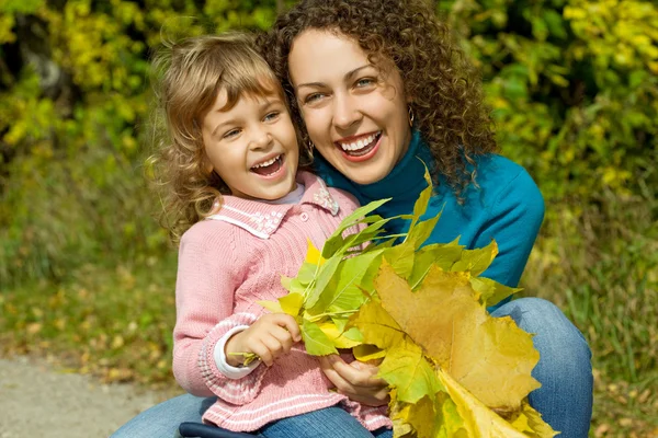 Mujer joven y niña se ríen con hojas en las manos en el jardín —  Fotos de Stock