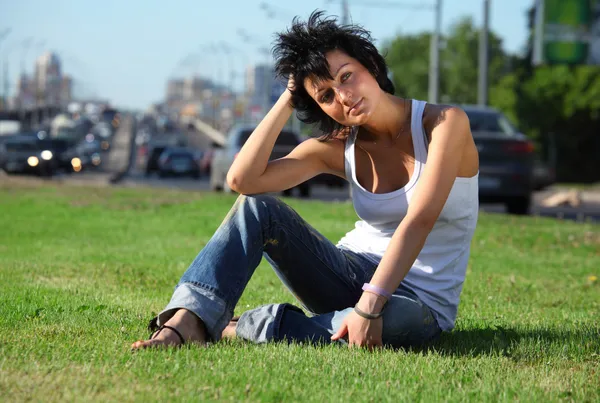 Dívka sedí na trávníku na silnici ve městě — Stock fotografie