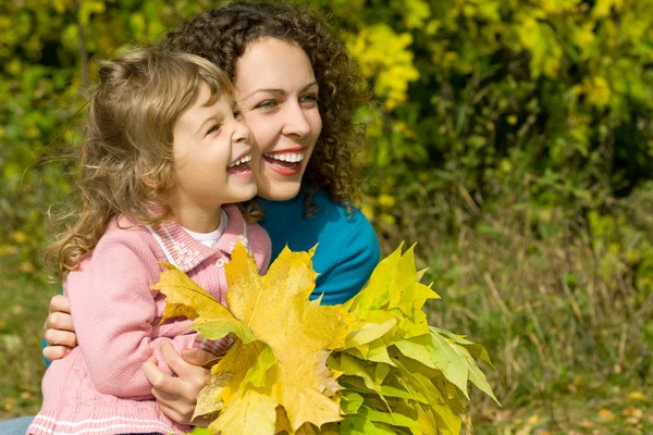 Young woman and little girl laugh with leaves in hands in garden — Stock Photo, Image