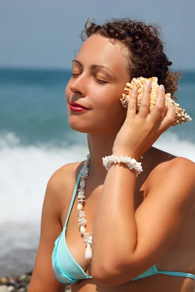 Beautiful woman has leant seashell bowl to an ear on seacoast — Stock Photo, Image
