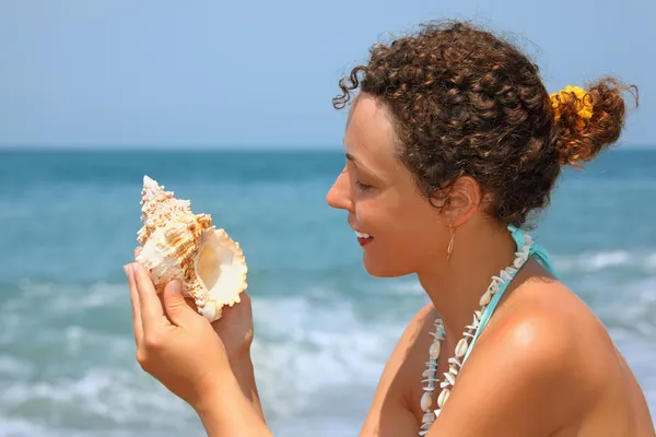 Bela mulher considerando concha na costa — Fotografia de Stock