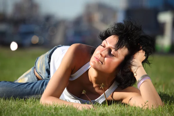 Dívka leží na trávníku na silnici ve městě — Stock fotografie