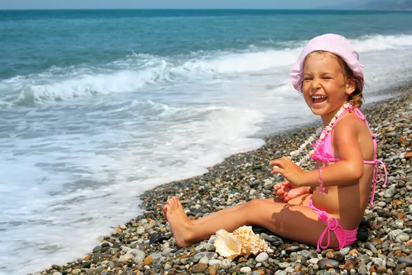 Graziosa bambina con conchiglia e collana sulla costa di pietra — Foto Stock