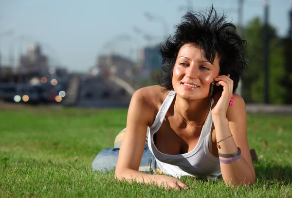 Girl lies on lawn at road in city and speaks by phone — Stock Photo, Image