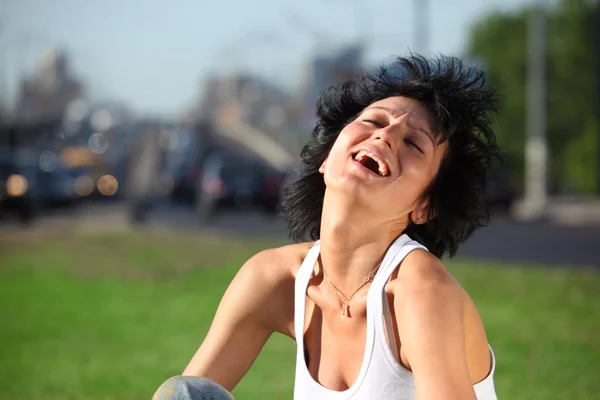 Laughing girl sits on lawn at road in city — Stock Photo, Image