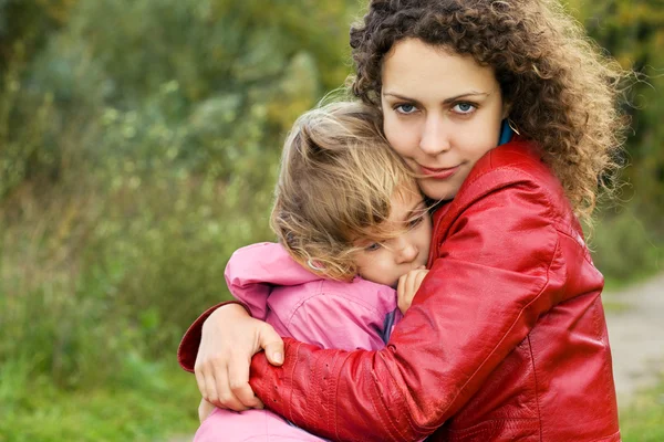 Young woman protects little girl from wind in garden — Stock Photo, Image