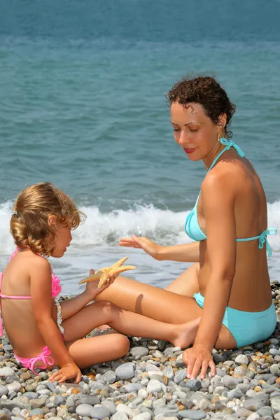 Młoda kobieta z małą dziewczynką rozegrane kamienista plaża rozgwiazda — Zdjęcie stockowe