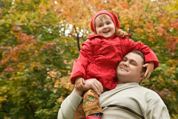 Küçük kız sonbaharda parkta erkeğin omzunda oturur. — Stok fotoğraf