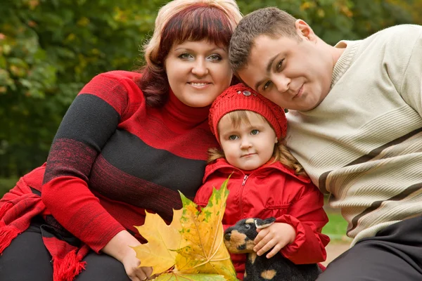 Married couple and little girl sit on a bench in park in autumn — Stock Photo, Image