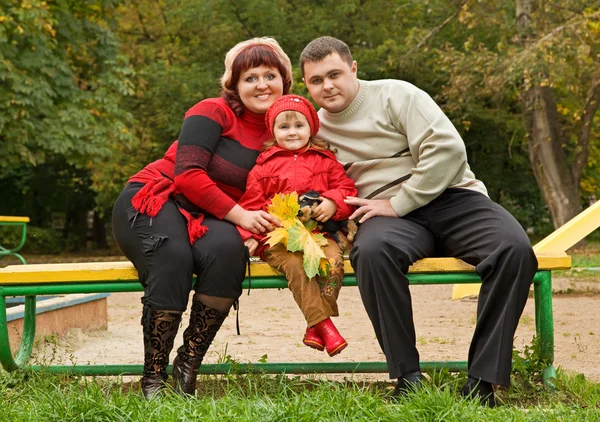 Pareja casada y niña se sientan en un banco en el parque en otoño —  Fotos de Stock
