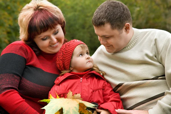 Married couple and little girl sit on a bench in park in autumn — Stock Photo, Image