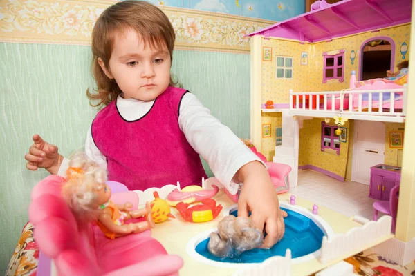 Little girl washes a doll in pool of toy house — Stock Photo, Image