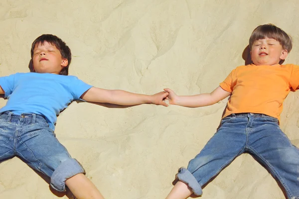 Два мальчика лежат на песке с закрытыми глазами — стоковое фото
