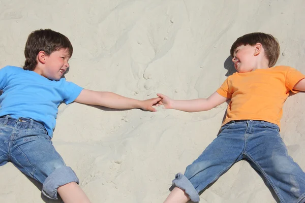 Two children lying nearby on sand look on each other — Stock Photo, Image
