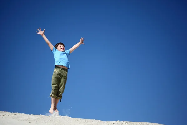 Menino pula na areia com as mãos levantadas — Fotografia de Stock