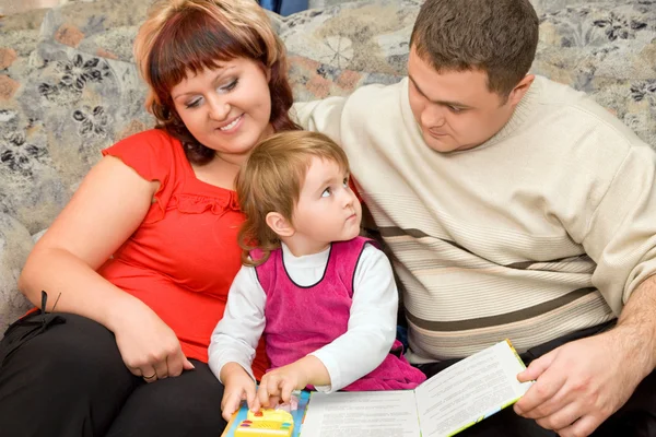 Married couple and little girl read book in a cosy room — Stock Photo, Image