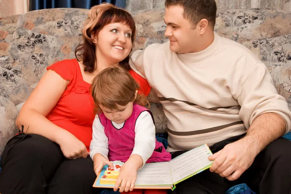 Ehepaar und kleines Mädchen lesen Buch in einem gemütlichen Zimmer — Stockfoto