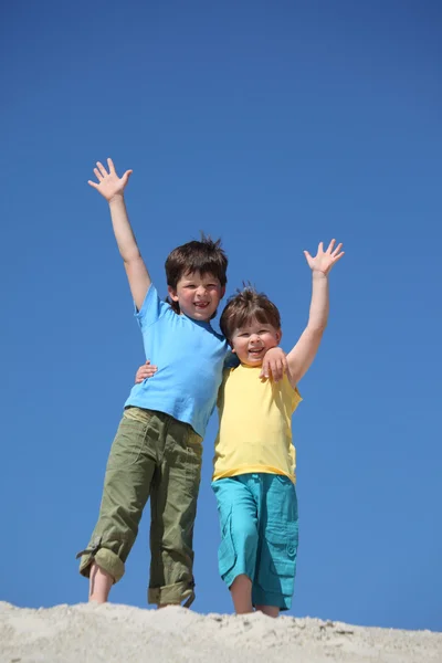 Dva chlapci stojí na písku a zvedl ruce v pozdravu — Stock fotografie