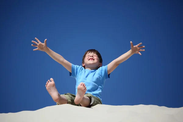 Chlapec sedí na písku s zdvižené ruce se zavřenýma očima — Stock fotografie