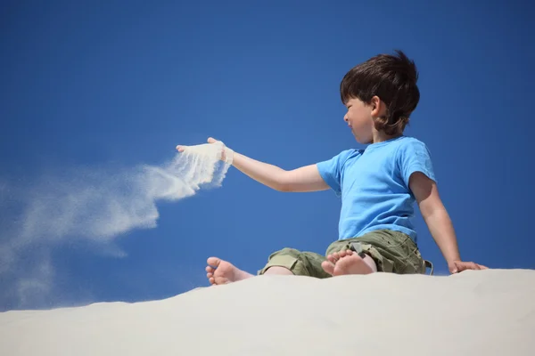 Niño se sienta en la arena y lo dispersa — Foto de Stock