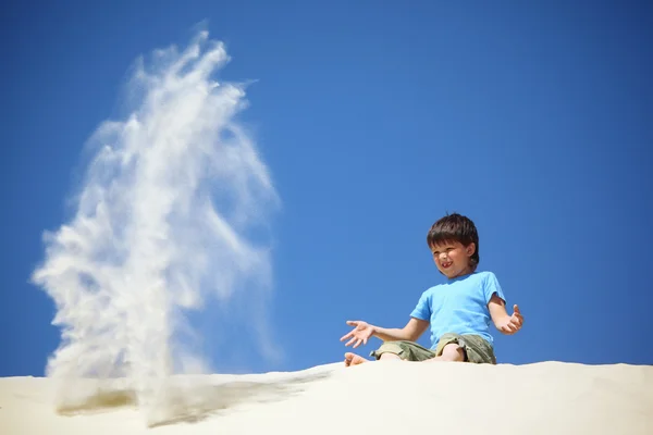 Chłopiec siedzi na piasku i rozprasza to — Zdjęcie stockowe