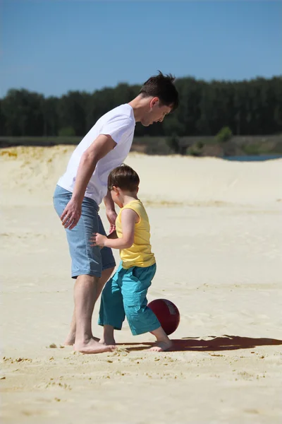 息子のいる父親は砂の上でサッカーを — ストック写真