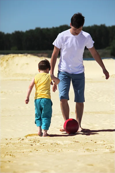 Отец с сыном играют в футбол на песке — стоковое фото
