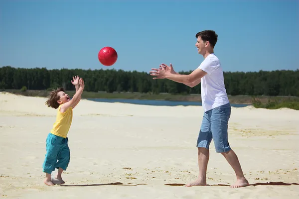 Син кидає м'яч батькові на пісок — стокове фото