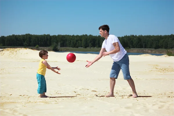 Father and son throw each other ball on sand — Stock Photo, Image