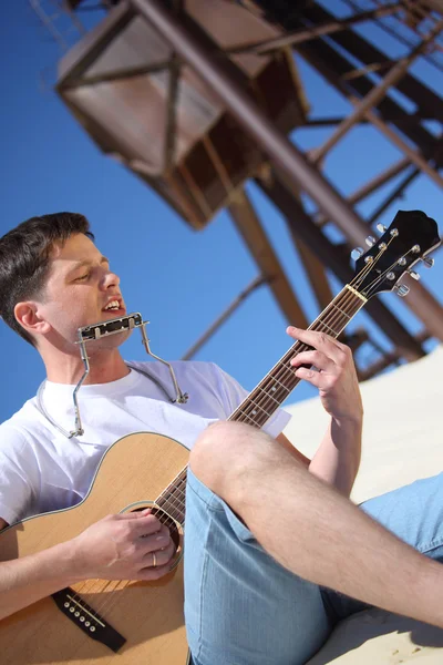 Ο τύπος παίζει κιθάρα και ακορντεόν στα χείλη καθισμένος στην άμμο — Φωτογραφία Αρχείου