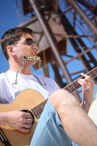 Guy in sunglasses plays guitar and lip accordion sitting on san — Stock Photo, Image