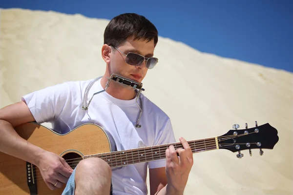 Güneş gözlüklü adam gitar ve dudak akordeon san üzerinde oturmuş oynar — Stok fotoğraf